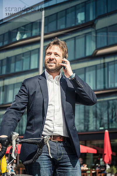 Geschäftsmann mit Fahrrad macht Smartphone-Anruf in der Stadt