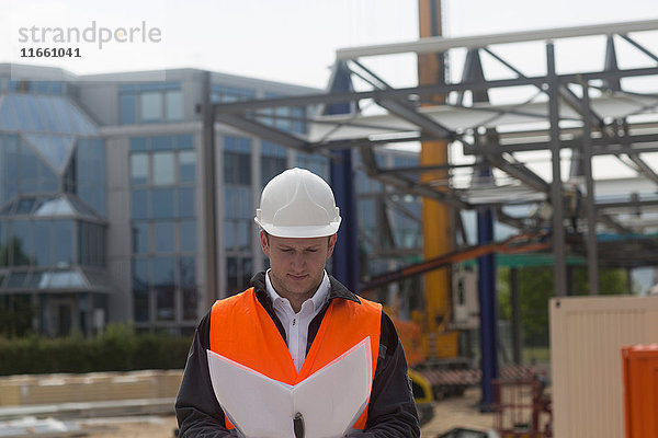 Junger männlicher Bauingenieur betrachtet Bauplan auf der Baustelle