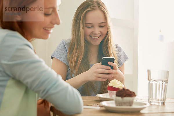 Mädchen im Cafe schaut auf Smartphone und lächelt