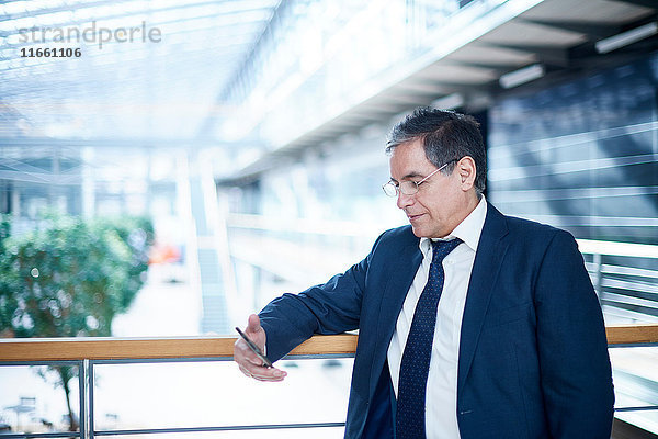 Reifer Geschäftsmann betrachtet Smartphone auf Bürobalkon