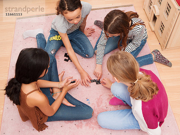 Mädchen sitzen auf dem Boden und spielen Domino