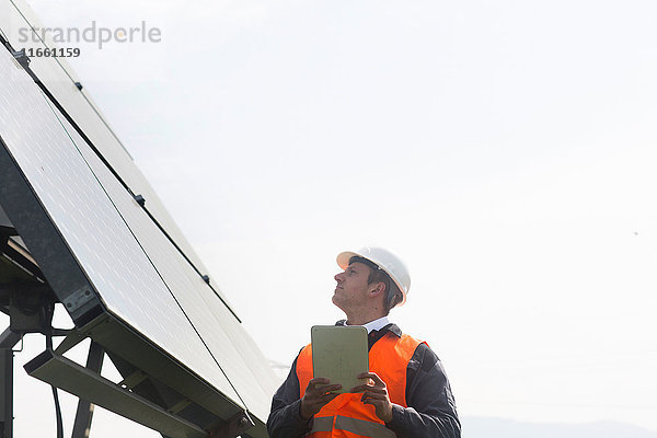 Junger männlicher Ingenieur mit digitalem Tablett schaut zu Sonnenkollektoren auf