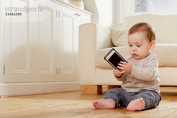 Kleiner Junge sitzt auf dem Boden und schaut auf ein Smartphone
