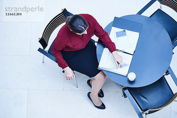 Draufsicht einer Geschäftsfrau  die am Tisch im Atrium des Büros Papierkram liest