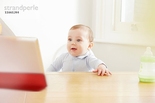 Kleiner Junge am Tisch mit Blick auf digitales Tablett