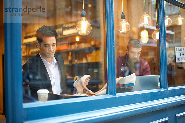 Fensteransicht von Geschäftsleuten  die Zeitung lesen und Laptop im Cafe benutzen