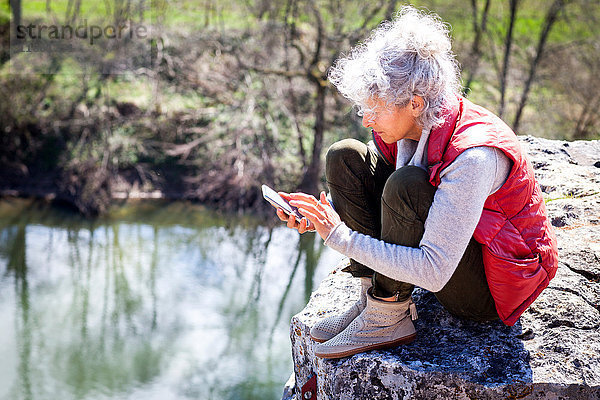 Frau sitzt auf einem Felsen und simst auf einem Smartphone  Bruniquel  Frankreich