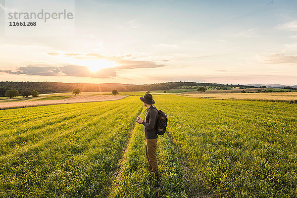 Mittelgroßer erwachsener Mann  im Feld stehend  eine Spiegelreflexkamera haltend  schaut ins Bild  Neulingen  Baden-Württemberg  Deutschland