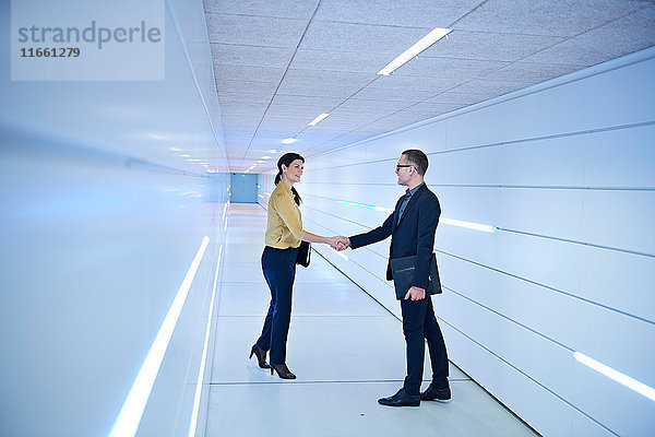 Geschäftsfrau und Mann schütteln Hände im Bürokorridor