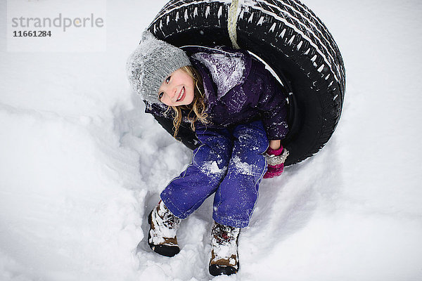 Portrait eines Mädchens auf Reifenschaukel im Schnee