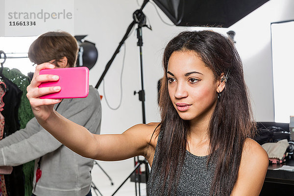 Junges weibliches Modemodel nimmt Smartphone-Selfie im Fotografenstudio