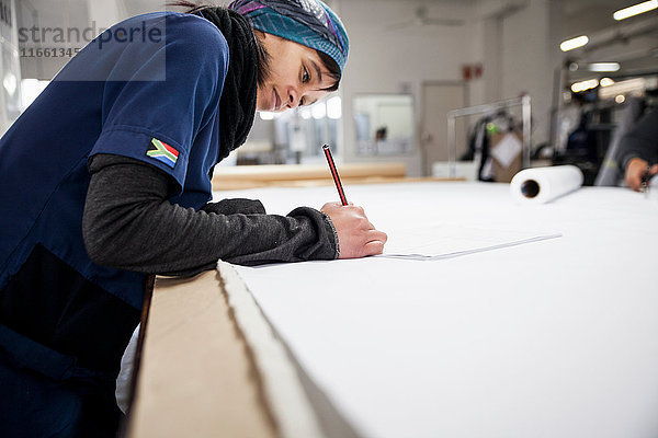 Fabrikarbeiter macht Notizen am Arbeitstisch in einer Bekleidungsfabrik