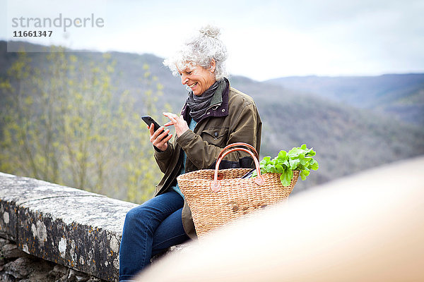 Frau sitzt an der Wand und schreibt SMS auf Smartphone  Bruniquel  Frankreich