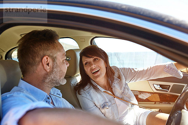 Ehepaar im Auto  Mann am Steuer  Frau zeigt nach vorne  lachend