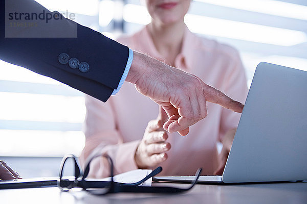 Ausschnitt eines Geschäftsmannes  der auf einen Laptop auf dem Bürotisch zeigt