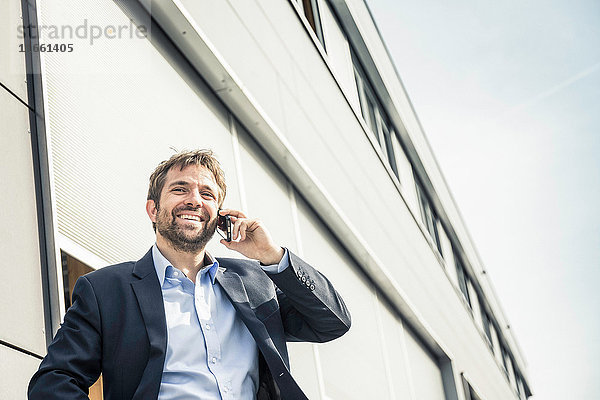 Geschäftsmann telefoniert mit seinem Smartphone vor dem Bürogebäude