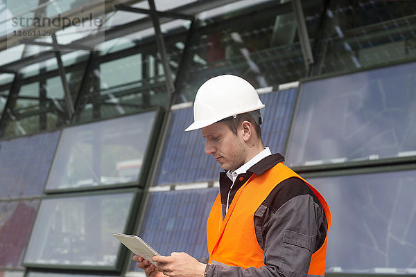 Junger männlicher Ingenieur betrachtet digitales Tablet am Standort eines Solarpanels