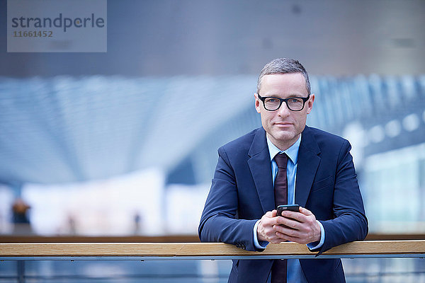 Porträt eines Geschäftsmannes mit einem Smartphone in der Hand auf dem Bürobalkon