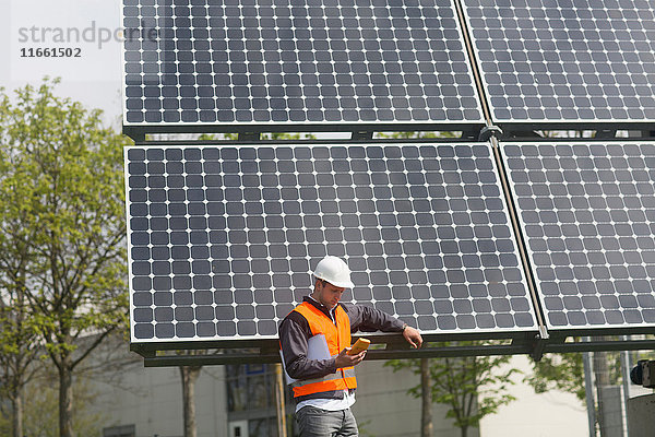 Männlicher Ingenieur betrachtet Multimeter am Standort der Solaranlage