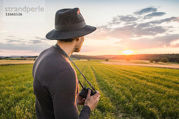 Porträt eines mittelgroßen erwachsenen Mannes  im Feld stehend  eine Spiegelreflexkamera haltend  auf Ansicht schauend  Neulingen  Baden-Württemberg  Deutschland