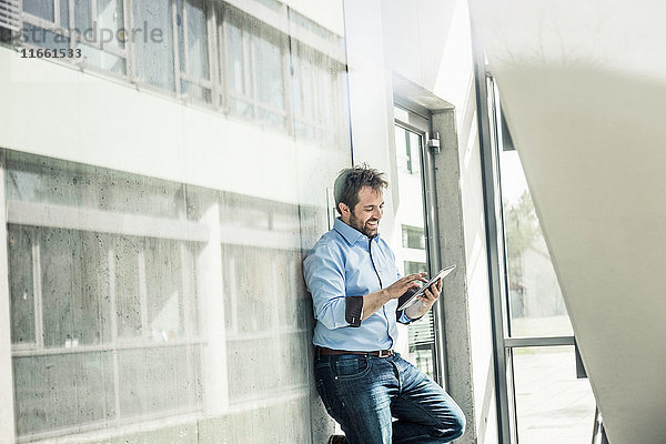 Geschäftsmann lehnt mit digitalem Tablet-Touchscreen an Büro-Lobby-Wand