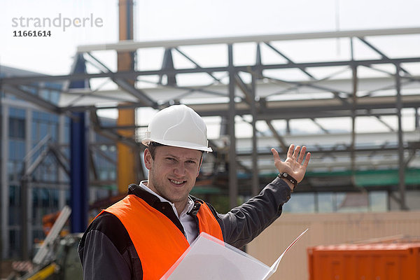 Porträt eines jungen männlichen Bauingenieurs  der auf der Baustelle ein Baugerüst zeigt