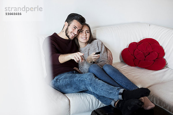Junges Paar entspannt sich auf dem Sofa  sieht fern  junge Frau hält Fernbedienung