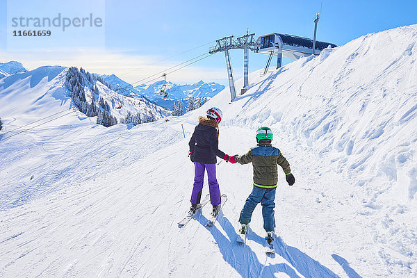Rückansicht eines Mädchens und eines Bruders  die sich auf der Skipiste an den Händen halten  Gstaad  Schweiz