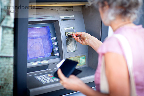 Reife Frau  die eine Kreditkarte in einen lokalen französischen Geldautomaten einführt