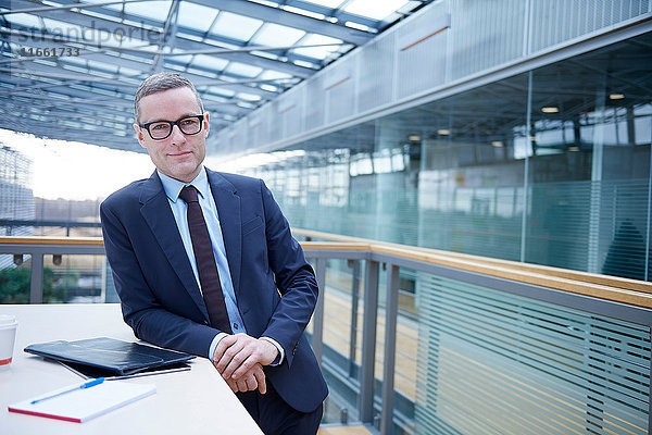 Porträt eines Geschäftsmannes  der sich an einen Balkontisch im Büro lehnt