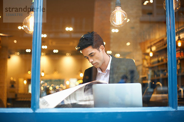 Fensteransicht des Geschäftsmannes beim Lesen von Broadsheet-News im Cafe