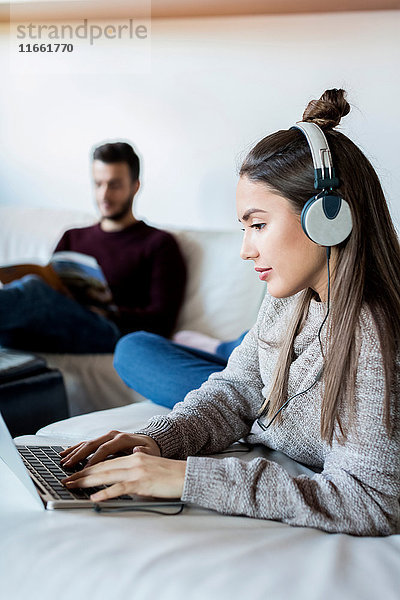 Junges Paar entspannt sich zu Hause  junge Frau benutzt Laptop  junger Mann liest Zeitschrift
