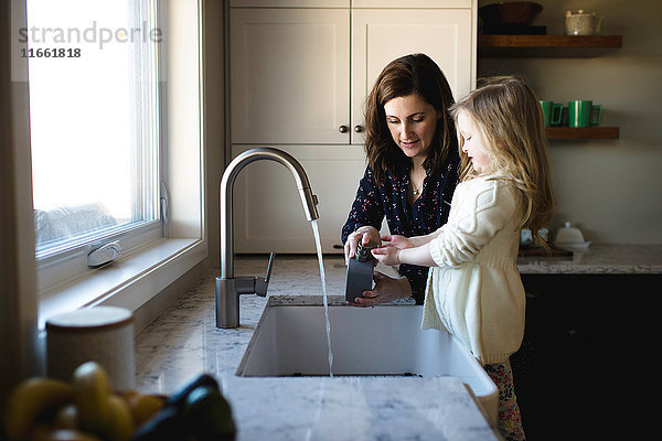 Frau hilft Tochter beim Händewaschen an der Küchenspüle