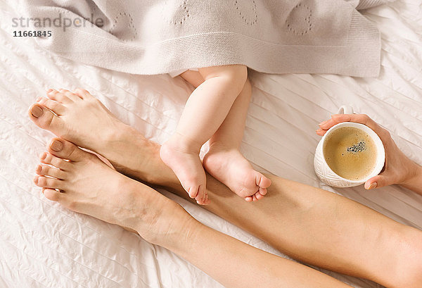 Mutter und Baby mit nackten Füßen auf dem Bett
