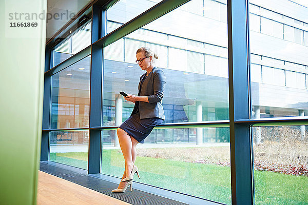 Geschäftsfrau schaut auf Smartphone am Fensterplatz im Büro