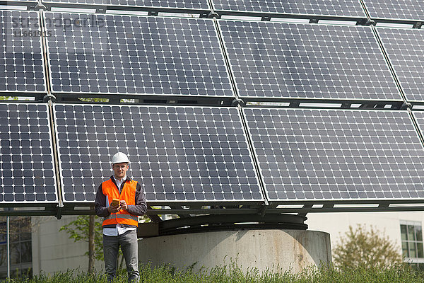 Porträt eines jungen männlichen Ingenieurs  der ein Multimeter am Standort eines Solarpanels hält