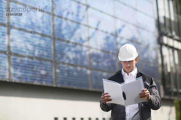 Männlicher Ingenieur schaut sich den Papierkram auf der Baustelle für Solarpaneele an