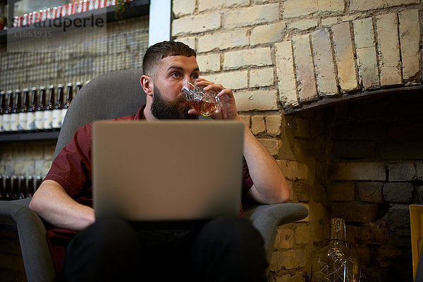 Junger Mann mit Laptop Trinkbecher des Geistes in der Gaststätte