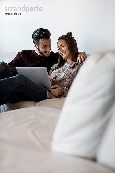 Junges Paar entspannt sich auf dem Sofa und schaut auf den Laptop