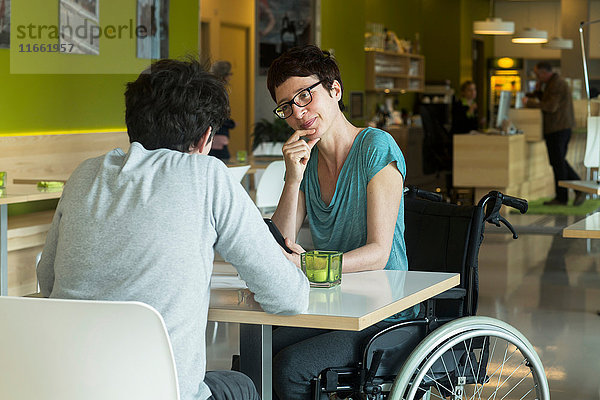 Frau im Rollstuhl  die mit einem Freund am Restauranttisch sitzt