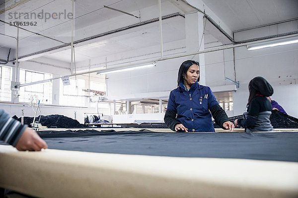 Fabrikarbeiter rollen Textilien auf Arbeitstisch in Bekleidungsfabrik aus