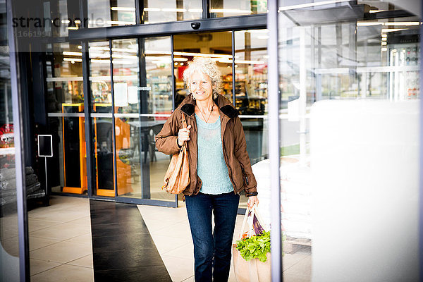 Reife Frau verlässt Supermarkt mit Einkaufstüte