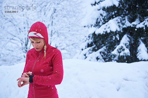 Läuferin in roter Kapuze kontrolliert Smartwatch im Schnee  Gstaad  Schweiz