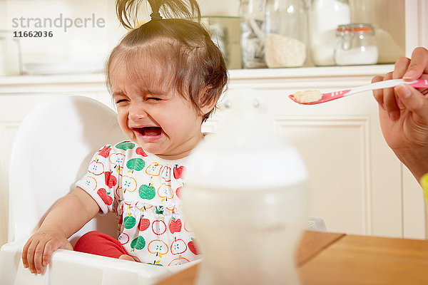Kleines Mädchen weint  während es von der Mutter mit Frühstück gefüttert wird