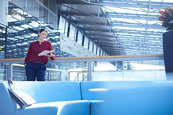 Geschäftsfrau liest Papierkram im Atrium des Büros