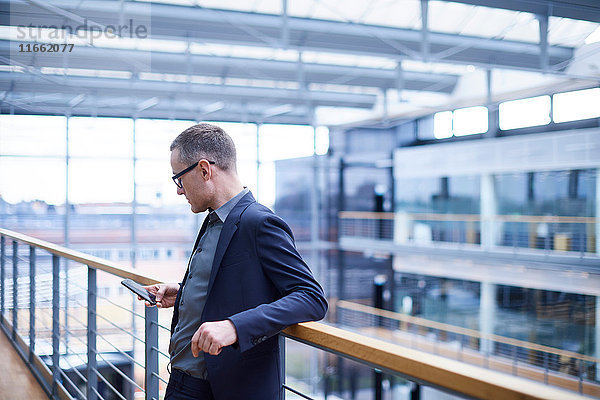 Geschäftsmann schaut auf Smartphone auf Bürobalkon