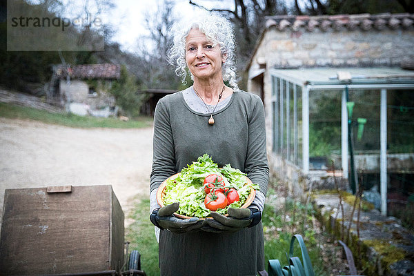 Porträt einer reifen Gärtnerin mit Schale mit Tomaten und Frühlingsgrün