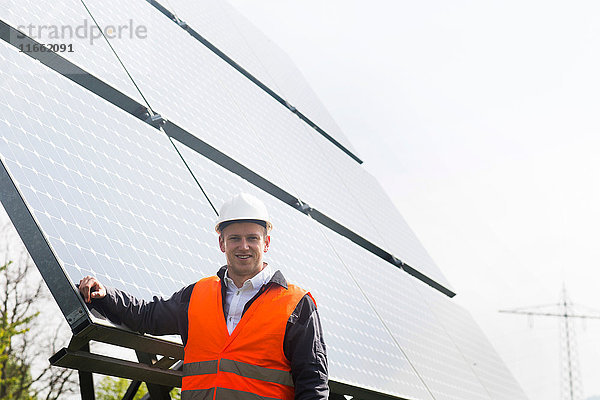 Porträt eines jungen männlichen Ingenieurs  der sich an ein Solarpanel lehnt