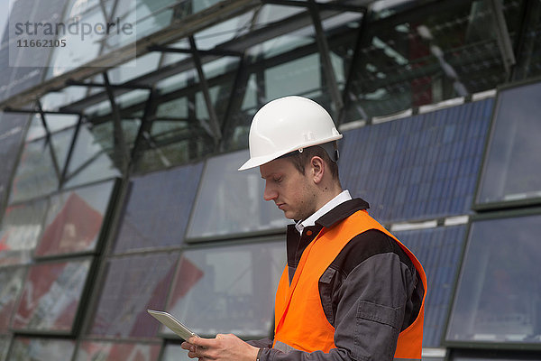 Junger männlicher Ingenieur betrachtet digitales Tablet am Standort eines Solarpanels