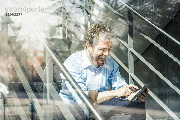 Bürofensteransicht eines Geschäftsmannes mit digitalem Tablet-Touchscreen auf der Treppe